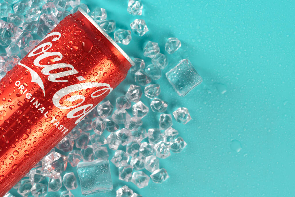 Cold can of Coca-Cola drink on blue background with ice